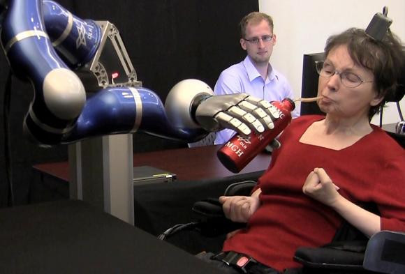 امرأة مصابة بشلل رباعي تستخدم ذراعا روبوتية يتحكم فيها الدماغ لرفع زجاجة إلى فمها.